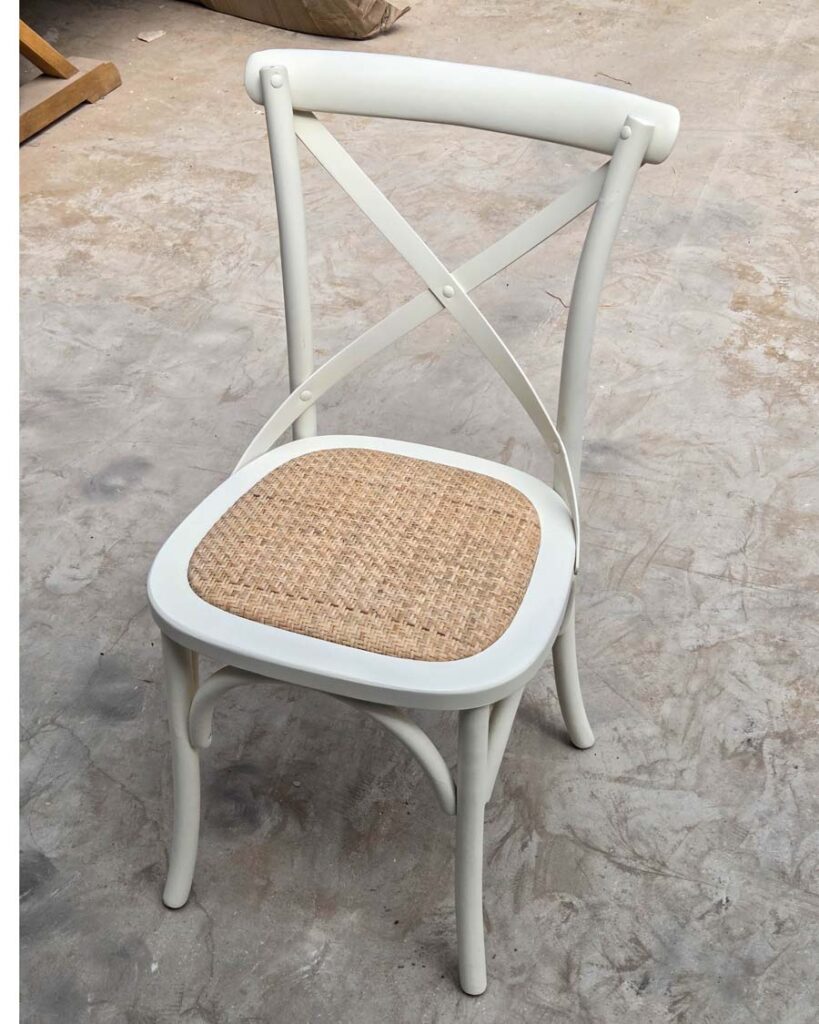 "כסא איקס (Cross-back) עשוי עץ מלא בצבע שמנת עם מושב ראטן קלוע טבעי, לפינת אוכל בסגנון כפרי מעוצב.