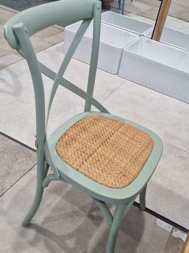כסא איקס (Cross-back) עשוי עץ מלא בצבע ירוק עם מושב ראטן קלוע טבעי, לפינת אוכל בסגנון כפרי מעוצב.